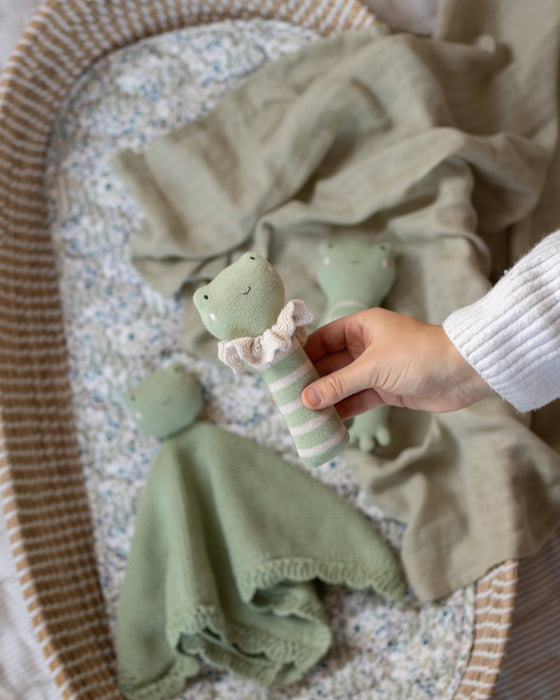Hand holding a green baby rattle near a crib with a blanket and baby comfort blanket.