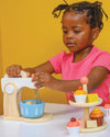 Child playing with a wooden kitchen set against a yellow background