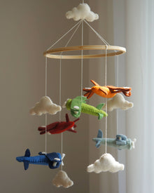  Children's mobile with airplanes and clouds hanging from a wooden ring against a neutral background.