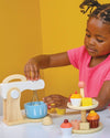 Child playing with a wooden kitchen set against a yellow background