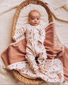 Baby in a floral onesie lying in a woven basket with pink blanket
