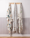 Three patterned baby blankets hanging on a wooden rack against a white wall with a wooden baseboard.
