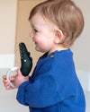 Child in a blue sweater holding a black plush toy and white object.