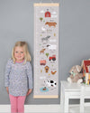 Child standing next to a growth chart with farm-themed illustrations on a gray wall.