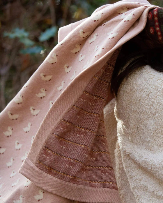 Close-up of a pink fabric with butterfly pattern draped over a person, with a blurred natural background.