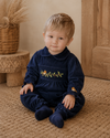 Child wearing a navy blue outfit with floral embroidery sitting on a carpeted floor.