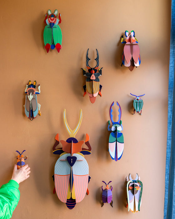 Colorful insect-shaped wall decorations on a beige wall with a person's hand reaching out.