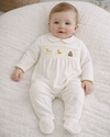 Baby in a white embroidered onesie lying on a textured white surface