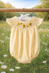 Yellow checkered baby romper with floral embroidery on a hanger against a natural background