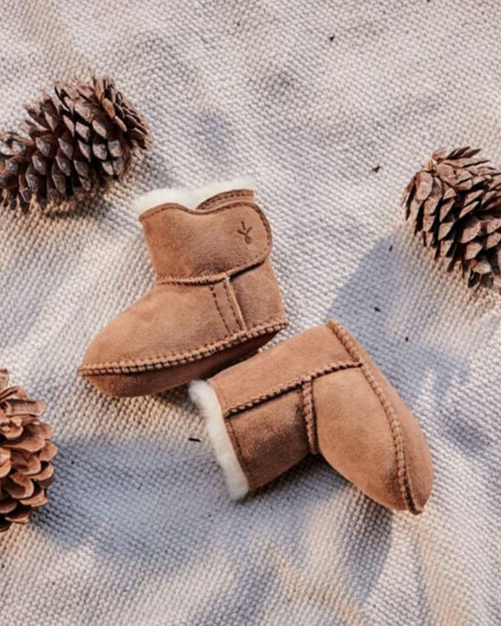 Pair of brown children's boots with white fur lining on a textured surface with pine cones.