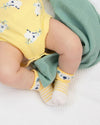 Baby wearing a yellow outfit with cow print, green pants, and yellow socks with white stripes on a white background.