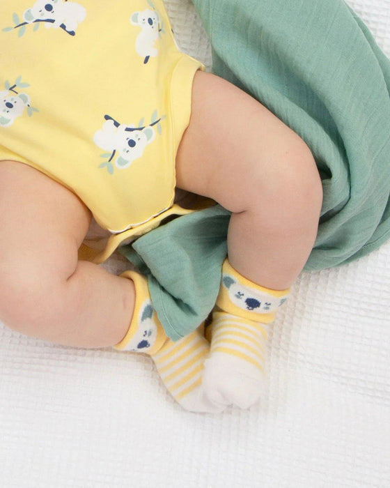 Baby wearing a yellow outfit with cow print, green pants, and yellow socks with white stripes on a white background.