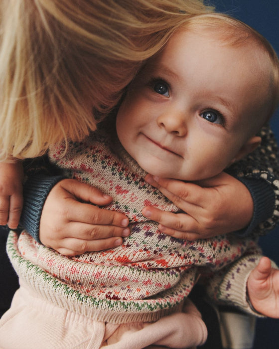 Child wearing a colorful sweater being held by an adult with a blue background