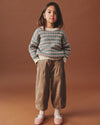 Young girl wearing a patterned sweater and brown pants on a brown background