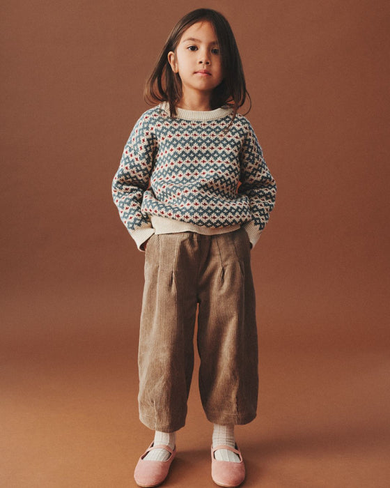 Young girl wearing a patterned sweater and brown pants on a brown background