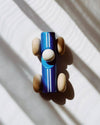 Wooden toy car with blue body and brown wheels on a white surface with shadows.