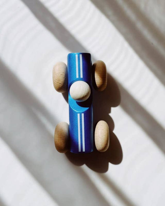 Wooden toy car with blue body and brown wheels on a white surface with shadows.