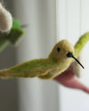 Felted yellow bird toy held by a hand with a blurred background