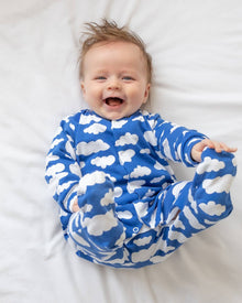  Baby wearing a blue onesie with white cloud patterns, lying on a white surface.