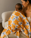 Woman holding a baby wrapped in a floral blanket on a couch.