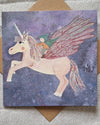 Card with a unicorn and fairy design on a textured surface