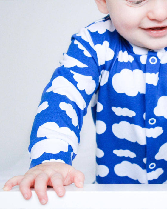 Baby wearing a blue onesie with white cloud patterns on a plain background