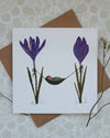 Greeting card with illustration of a baby in a hammock between purple flowers, on a textured surface.