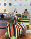 Knitted dog toy in front of striped candles and a polka dot wall.
