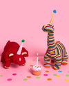 Two knitted dinosaur toys with party hats on a pink background with colorful confetti.