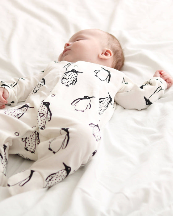 Baby wearing a onesie with penguin pattern lying on a white surface