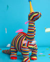 Colorful knitted dinosaur toy on a blue background with confetti