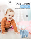 Baby playing with a blue elephant rattle on a soft surface with flowers and a blurred background.