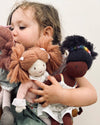 Child holding three dolls with different hairstyles against a plain background