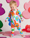Child wearing a colorful floral onesie with a playful background of oversized flowers.