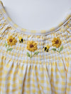 Yellow and white checkered fabric with embroidered sunflowers and bees on a plain background