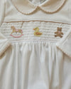 Close-up of a white garment with embroidered animal designs on a beige background