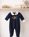 Navy baby onesie with 'ABC' on a hanger against a white wall with toys in the background