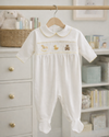 White baby romper with embroidery on a hanger in a nursery setting