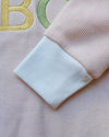 Close-up of a textured fabric with embroidered letters on a light pink background