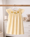 Yellow checkered dress with floral embroidery on a hanger in a nursery.