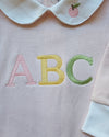 Embroidered letters 'ABC' on a baby outfit with a bib.