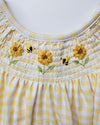 Yellow and white checkered fabric with embroidered sunflowers and bees on a plain background
