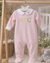 Pink baby onesie with 'ABC' letters on a wooden rack in a nursery setting.