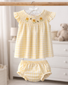 Yellow checkered baby dress with bloomers hanging on a rack in a nursery.