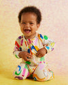Child wearing a colorful outfit with a pattern of letters and shapes on a light pink background