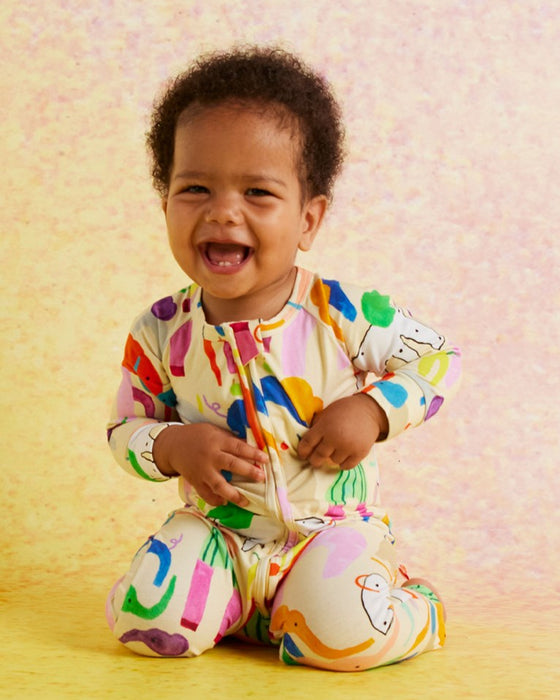 Child wearing a colorful outfit with a pattern of letters and shapes on a light pink background