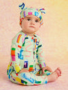 Baby wearing a colorful outfit with a pattern of letters and numbers on a soft pink background