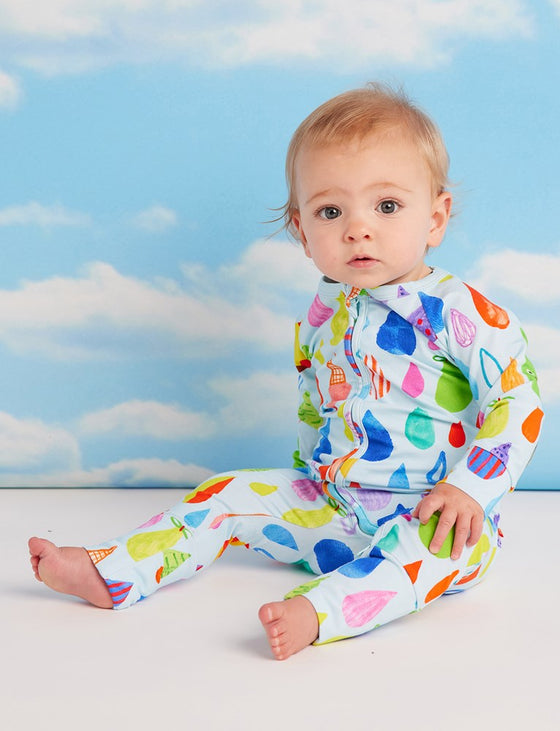 Baby wearing colorful pajamas with a pattern of balloons against a blue sky background