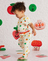 Child in a colorful outfit standing on a patterned floor with cartoonish vegetables and fruits.