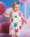 Child wearing a colorful floral dress against a whimsical background with fluffy pink clouds and a blue sky.